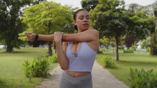 Young Woman Stretching Arms in Lush Urban Park
