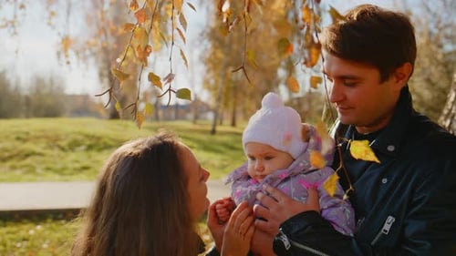 A Joyful Family Moment Parents Cherishing Their Baby Under Autumn Leaves in a Serene Park Setting