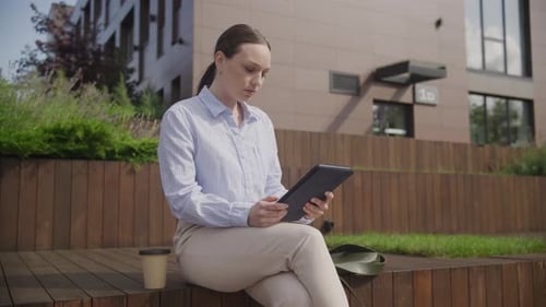 Woman Uses Tablet Sitting Outside in Urban Setting