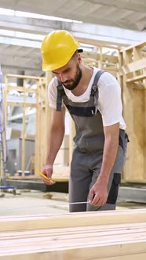 Debout, marquant la planche au crayon. Ouvrier industriel dans un entrepôt en bois.