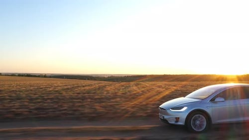 Electric Car Driving on a Rural Road at Sunset