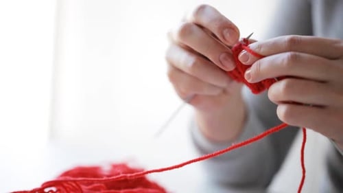 Woman Knitting Red Yarn with Needles Indoors
