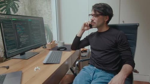 IT Programmer Looking at Computer Code and Calling on Phone
