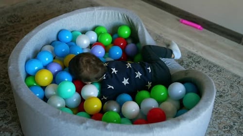 Adorable active toddler jumps into the dry basin with balls. Happy funny kid deepens into the toys.