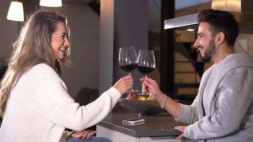 Two young people with a glass of wine in a romantic evening in the kitchen of their home, lifestyle