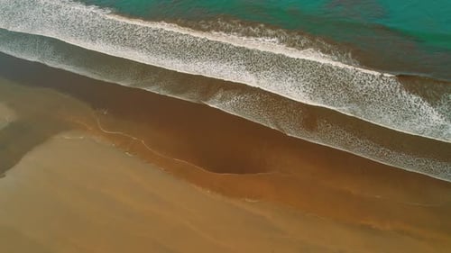 Aerial view of long rolling ocean waves on dark sand in Costa Rica