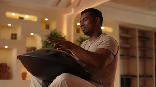 Side View of Relaxed Black Male in Trance Playing on Glucophone with Closed Eyes Sitting on Floor in