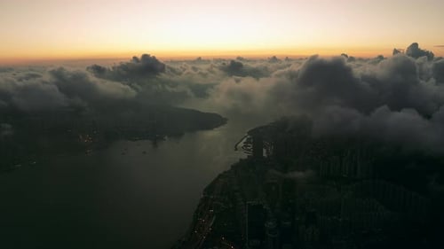 Dark silhouette of urbanisation under slowly moving dense clouds before sunrise. High altitude drone