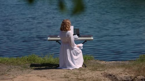 Back View Teen Caucasian Girl Sitting at Piano Synthesizer at Background of Blue River Water on