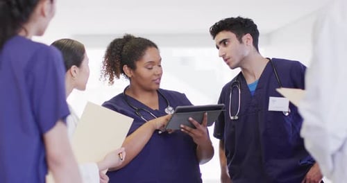 Video of diverse group of male and female doctors looking at tablet talking in hospital corridor