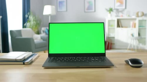 Zoom in on a Modern Laptop with Green Mock-up Screen Display Standing on the Desk of the Cozy Livin