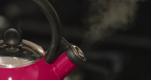Close up of a red tea pot bursting with steam indicated the water is boiling. The tea kettle is whis