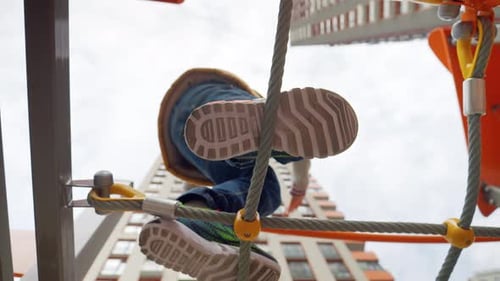 Happy smiling boy crossing the rope bridge on the playground at new city block