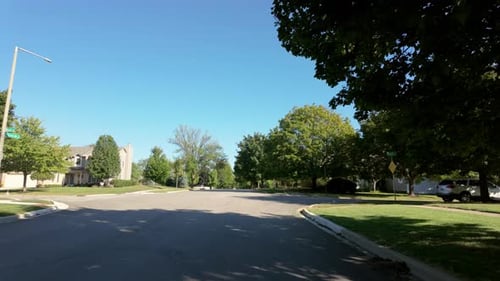 A Wide Pointofview Shot Taken From a Moving Car Capturing a Residential Neighborhood Near a Park in