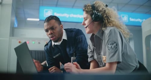 Airport Security Checkpoint Multiethnic TSA Officers in Headset Using Laptop Computer and Talking