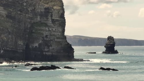 Aerial shot flying over quiet waters along a coastline with cliffs and rocks on a cloudy day