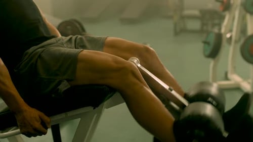 Homem forte de closeup com pernas treinando na academia. Homem de fisiculturismo irreconhecível fazendo extensão
de perna