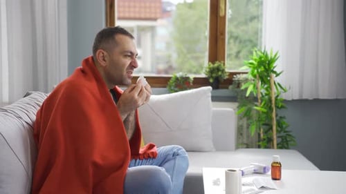 Man Sick with Cold Sits on Couch Sneeze