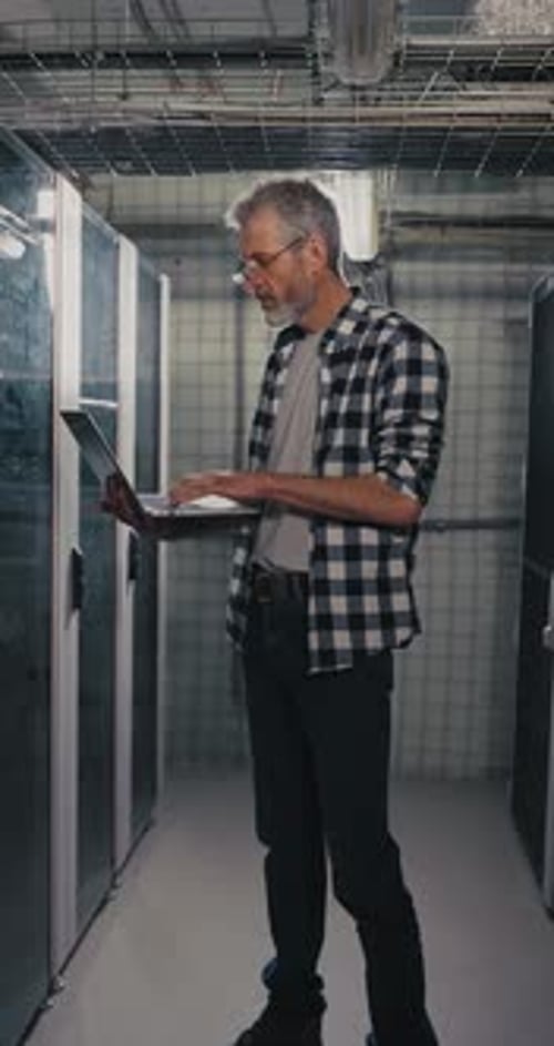 Man Works on Laptop in Dark Server Room
