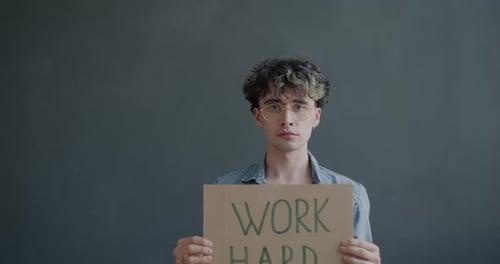 Schild mit Bildnis eines seriösen jungen Mannes, der Arbeitshärte hält, vor grauem Hintergrund