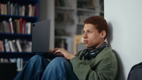Estudiante masculino birracial enfocado que trabaja en una computadora portátil en la biblioteca de la universidad