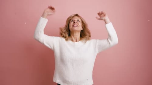 Woman Celebrates as Confetti Falls Against Pink Backdrop