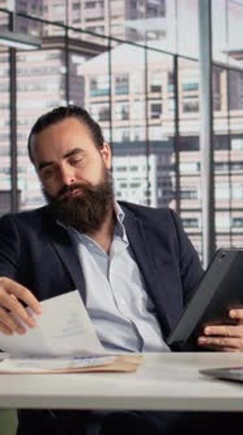 Vertical Video Business Leader Factchecking Documents with Company Data and KPIs on Tablet