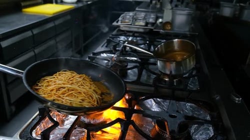 Close-up of a Restaurant Chef Cooking Food on Fire in the Restaurant Kitchen