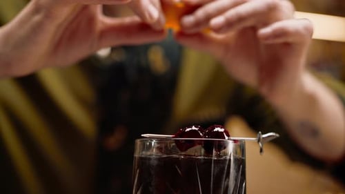 Nahaufnahme: Ein Barkeeper fügt einem frisch zubereiteten schwarzen alkoholischen Cocktail an der Bar eine Orangenscheibe hinzu