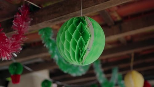Colorful decorations for a Popular Saints party, featuring hanging green and red paper ornaments and
