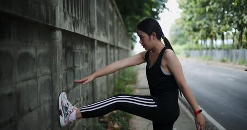 Young Woman Stretching Leg Against Wall Outdoors