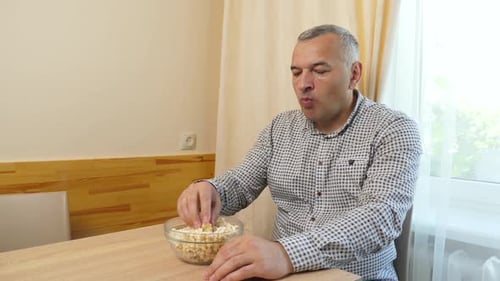 Man Eats Popcorn at Table Indoors