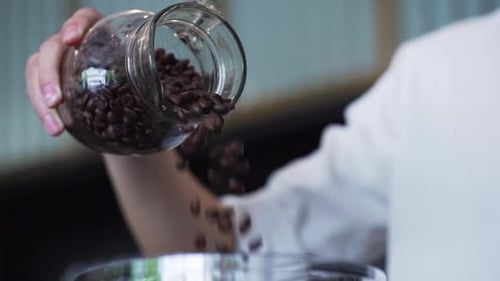 Barista pouring coffee beans from glass jar into hopper of espresso in cafe. Coffee making process.