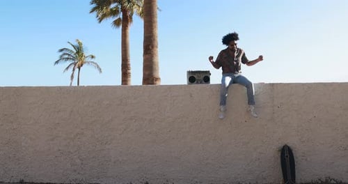 Man Dances by Boombox on Wall in Tropical Setting