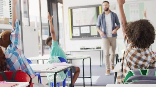 Diverse male teacher and happy schoolchildren at desk in school classroom
