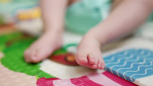Tiny feet of a baby lying on the bed on his back. Child lies calmly on a colorful cover. Close up.