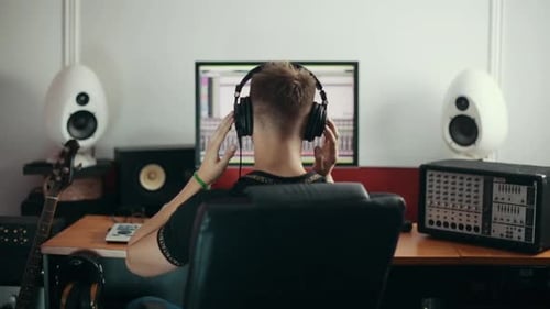Young sound engineer listening to the music in headphones and turning face back to the camera