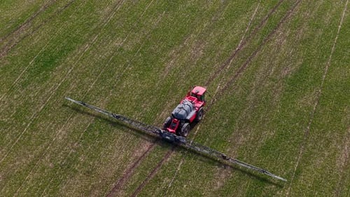 Aerial drone view of agricultural machinery spraying the field and working the land