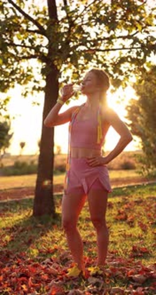 Happy woman drinking water outdoors in autumn park