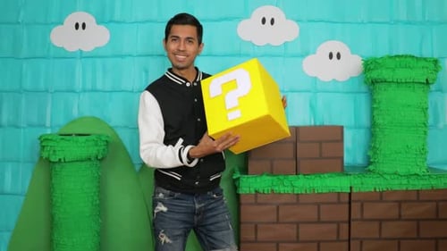 Man interacts with yellow cube in colorful video game-themed setting with cloud backdrops