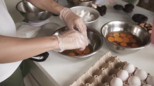 Baker's Hands Cracking Eggs Into Stainless Mixing Bowl. Baking In The Kitchen. close up