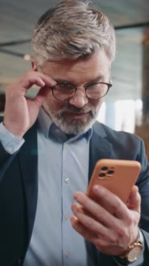 Closeup Shooting of Positive Handsome Caucasian Man with Gray Beard Holding Mobile Phone in Hands