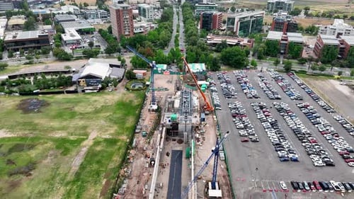 Zumbido aéreo delantero de una obra de construcción urbana con grúas, amplio estacionamiento con automóviles y