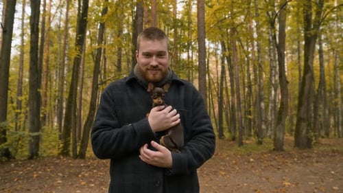 Portrait of Man Holding Brown Puppy in Autumn Forest Park