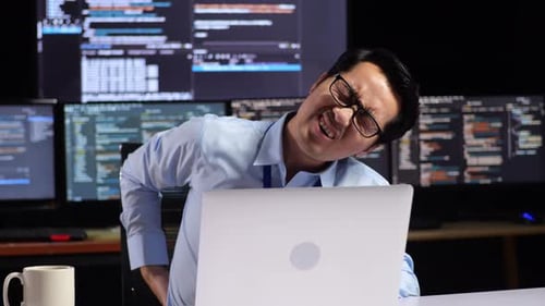 Asian Male Programmer Having A Backache While Writing Code By A Laptop Using Multiple Monitors