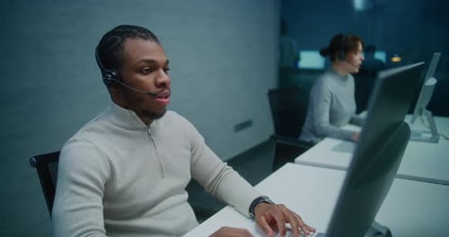 African American Helpdesk Specialist Talks on Headset with Customer Works on Computer