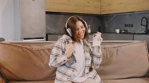 Woman Joyfully Dancing on Couch With Headphones