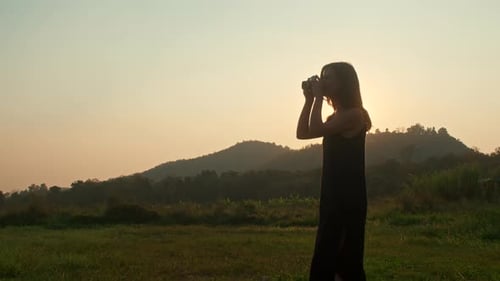 Woman Taking Pictures in Field at Sunset