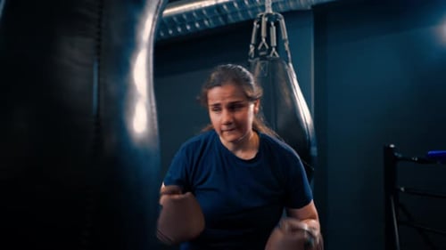 a girl boxer in gloves works out the power of punches on a punching bag in the gym trains hard