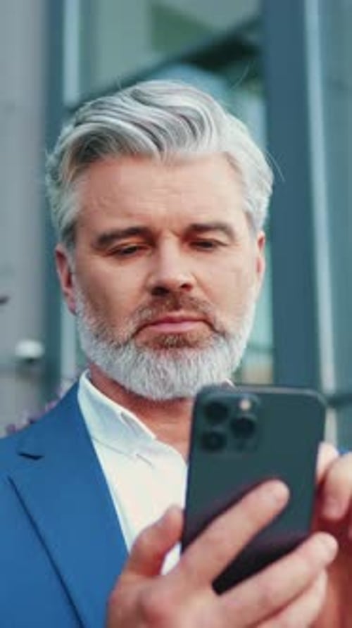 Close Up of Adult Man with Surprised Expression and Smiling Holding Smartphone in Hands Looking at